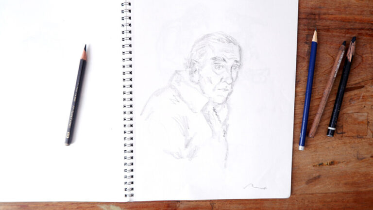Cuaderno de dibujo abierto con un retrato a lápiz y materiales de trabajo